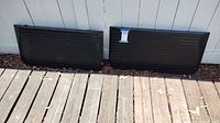 Two black heavy rubber wheelchair ramps leaning against an outdoor wall on a wooden deck, showing their length and width.