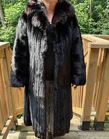 Front view of full-length black mink fur coat on model standing on outdoor deck