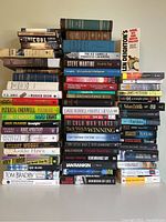 Photo showing an assortment of mixed hardcover and paperback books stacked and arranged horizontally and vertically, titles visible from various well-known authors in fiction and non-fiction.
