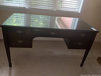 Front view of English style desk with glass top, showing five drawers and spade feet.