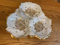 Porcelain condiment dish showing three divided sections with gold floral patterns and scalloped gold-trimmed edges with central handle.