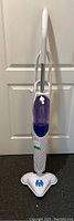 Front view of the full H2O mop steam cleaner showing white and purple body, handle and power cord wrapped on the side.