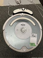 Top view of iRobot Roomba robotic vacuum with charging dock and power cable visible, showing wear and dust marks.