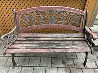 Front view of weathered iron garden bench with decorative floral cast iron back and wooden slats seat showing wear and peeling paint.