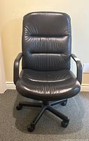 Front view of black leather office chair on wheels showing padded backrest and seat with armrests.