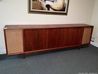 Front view of long mid century teak stereo credenza with two speaker grill panels at each end and four solid teak doors in the center.