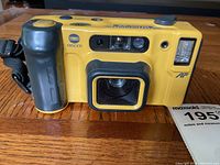 Front view of yellow Minolta Weathermatic Dura 35 camera showing lens, flash, grip, and brand markings.