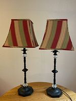 Pair of candlestick-style table lamps with striped fabric lampshades and black metal bases with clear glass accents.