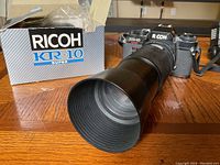 Full view of Ricoh KR-10 Super camera with Tamron 70-210mm f/4 lens and original Ricoh KR-10 Super box behind on a wooden surface.