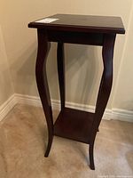 Full view of small dark wood side table with marks on the top surface, curved legs and a lower shelf.