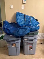Photo showing five large Rubbermaid storage bins stacked with lids, with three large blue IKEA bags on top.