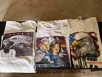 Three vintage political T-shirts laid out on a carpeted floor showing front designs.