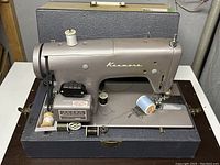 Full view of the vintage Kenmore sewing machine in its case with multiple spools of thread visible