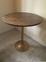 Front angle view of vintage oak veneer round table with metal pedestal base on carpeted floor near corner walls.
