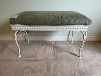 Front view of vintage wrought iron bench with green velvet upholstered seat on carpeted floor against a plain wall.