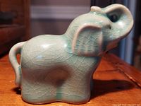 Side view of celadon elephant showing jade green crackle glaze and curled trunk.