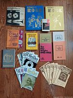 Top-down photo showing all items laid out on wooden floor including booklets, magazines, pamphlets, and small cassette/tape.