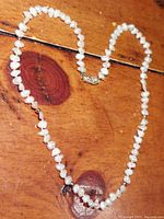 Full view of the entire necklace laid out on a wooden surface, showing the rice pearls and the overall length.