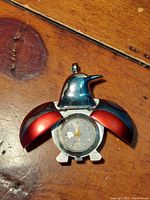 Photo showing the pendant watch open with wings spread revealing watch face on wooden surface.