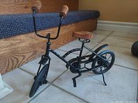 Side front view of the miniature vintage bicycle showing wood grips, metal frame, articulated pedals, and chain mechanism.