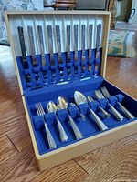 Wide view of the open wooden case with blue velvet lining containing the full set of vintage silver-plated cutlery including knives, forks, spoons, and a pepper shaker.