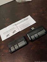 Two black garage door remotes with three buttons each shown with folded instruction sheet.