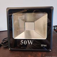 Front view of the UV flood lamp showing 50W and IP66 markings on glass and visible LED diodes inside.