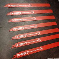 Seven red Diablo brand 12 inch automotive dismantling saw blades arranged side by side on a black surface, showing the full length and branding.