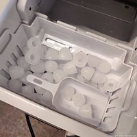 Open ice compartment showing multiple hollow rounded ice cubes and a white plastic scoop inside the ice basket.