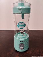 Full front view of the portable rechargeable blender showing mint green base, button, clear blending jar with BPA-free sticker and stainless steel blades inside.