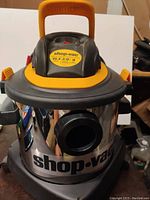 Front view of Shop-Vac showing stainless steel tank, black and yellow top, and front suction inlet.