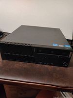 Front and top angled view of Lenovo ThinkCentre PC case showing power button, optical drive slot, ventilation grills, and certification stickers.