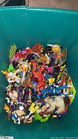 Top view of green plastic tote box filled with various action figures, mixed poses and colors.