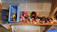 Wide shot on bench showing blue crate with small green army men, gray crate with plastic weapons, row of troll figures, small troll dolls, Furby parts and other toys