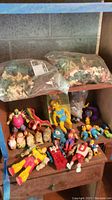 Photo showing two sealed bags of plastic army men on top shelf and various Simpsons and other plastic action figures on lower shelves.