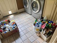 Wide view showing multiple boxes and buckets filled with assorted cleaning liquids, scotch guard, and other bottles.