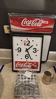 Front view of Coca-Cola plastic clock with white face, black numbers and hands, Coca-Cola dry erase board, metal stein, and jalapeño grill rack.