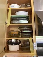 Open cabinets showing assortment of Corning glass bakeware, storage containers, and stainless steel bowl