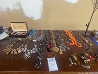 Photo of multiple vintage costume jewelry necklaces and earrings arranged on a wooden surface showing a variety of styles, colors, and materials including beads and rhinestones.