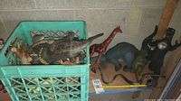Crate and loose plastic dinosaur and animal toys including giraffe, quadruped dinosaur figures, and Godzilla-like figures