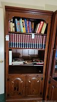 Full view of wooden Ethan Allen bookcase containing books on three shelves and closed double doors below.