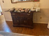 Front facing view of vintage Ethan Allen wooden server with varied serving dishes and glassware on top.