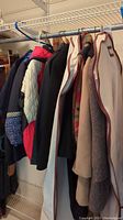 Photo showing multiple jackets and winter coats hanging on a rack, various colors and textures visible