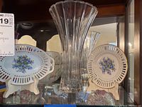 Display of two blue floral porcelain dishes flanking a tall clear crystal vase