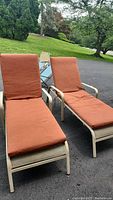 Two adjustable patio lounge chairs with beige metal frames, mesh seats, and orange cushions shown outdoors. Cushions appear slightly dirty and frames show paint chipping.
