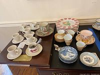 Overview of the lot showing various cups, saucers, plates and spoons arranged on two tables