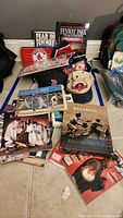 Photo shows various Boston Red Sox books, caps, and memorabilia arranged on floor including prominent books titled 'Fear In Fenway' and 'Fenway Park: A Stadium Like No Other'.