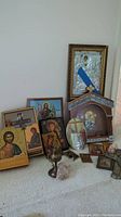 Overview of collected religious wall art with framed crosses, icons, and brass incense holder. Visible taped crack on one frame.