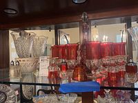Full display of the set inside a glass cabinet including bowls, ruby glassware, decanter, salt and pepper shakers, and bell.