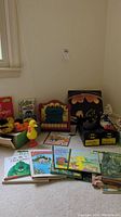Photo showing vintage Sesame Street toys, plush slippers of Bert and Ernie, a Cookie Monster musical keyboard toy, Big Bird figurine, and various children's books including dinosaur themes.